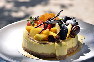 Image of a plain cheesecake, topped with fresh mango, banana, pineapple, 
                    chocolate swizzles and swirls