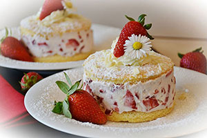 2 plates with a small strawberry cake on each, dusted with icing sugar,
                   garnished with strawberries and a daisy.